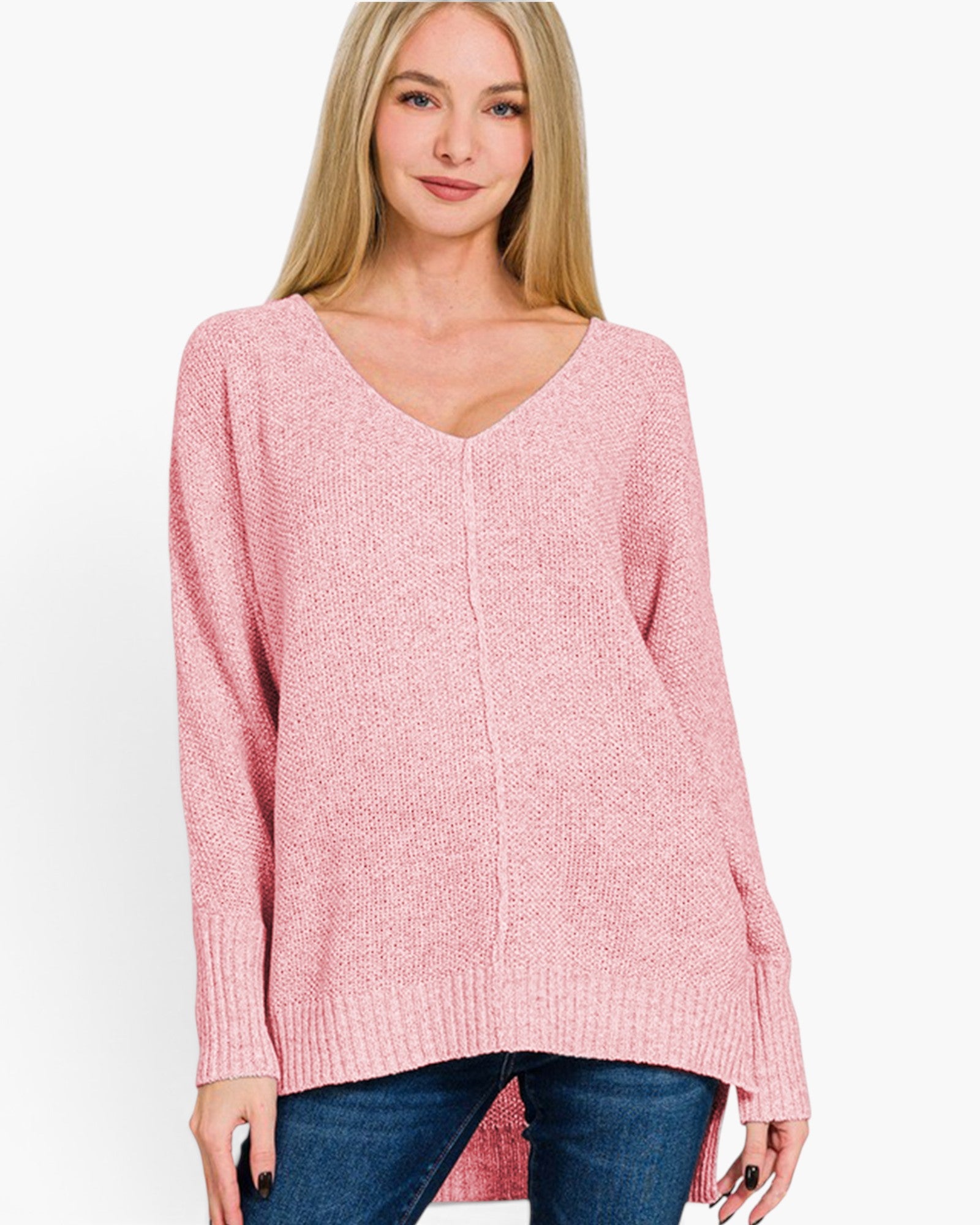 A woman wearing a pink knit sweater with a V-neck and long sleeves, paired with blue jeans, against a plain white background.