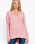 A woman wearing a pink knit sweater with a V-neck and long sleeves, paired with blue jeans, against a plain white background.