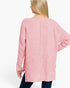A woman shown from the back wearing a pink knit sweater with a wide boat neckline, long sleeves, and a relaxed fit, paired with dark blue jeans against a plain white studio background.