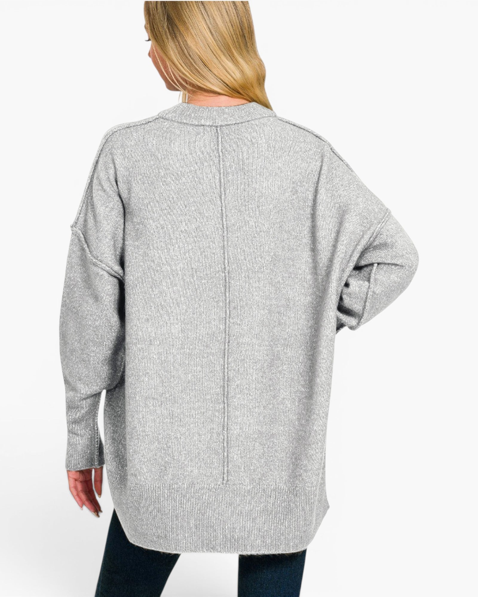 A woman viewed from the back wearing an oversized light gray ribbed knit sweater with long sleeves and a straight hem, paired with dark jeans against a plain light background.