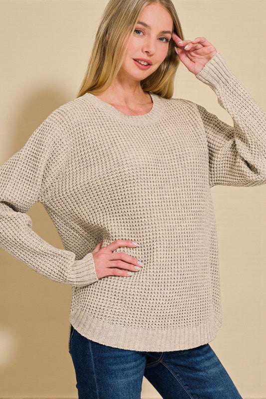 Woman wearing a beige knitted sweater and blue jeans against a beige background