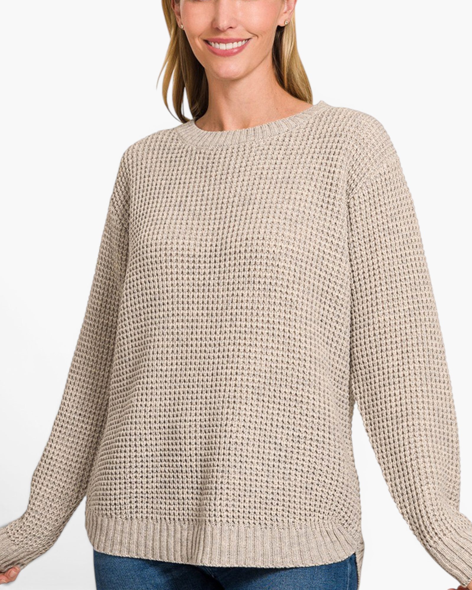 A woman wearing a beige waffle-knit crewneck sweater, paired with blue jeans, against a plain white background.