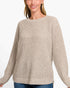 A woman wearing a beige waffle-knit crewneck sweater, paired with blue jeans, against a plain white background.