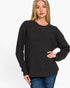 A woman wearing a dark charcoal gray waffle-knit crewneck sweater and blue jeans, standing against a plain white studio background.