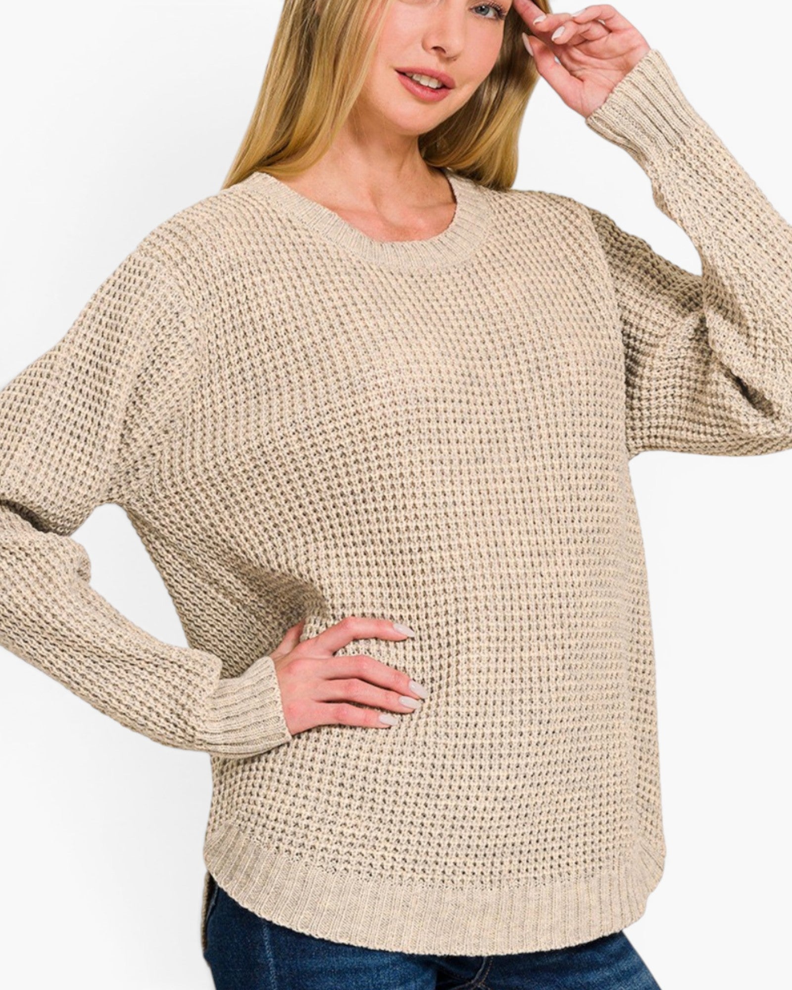 A woman wearing a beige waffle-knit long-sleeve sweater with blue jeans, shown from the chest down against a plain white background.