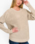 A woman wearing a beige waffle-knit long-sleeve sweater with blue jeans, shown from the chest down against a plain white background.