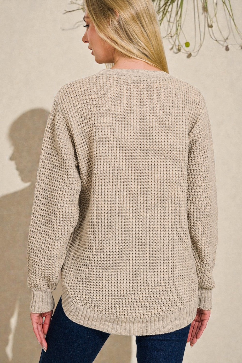 Woman wearing a beige knitted sweater against a neutral background