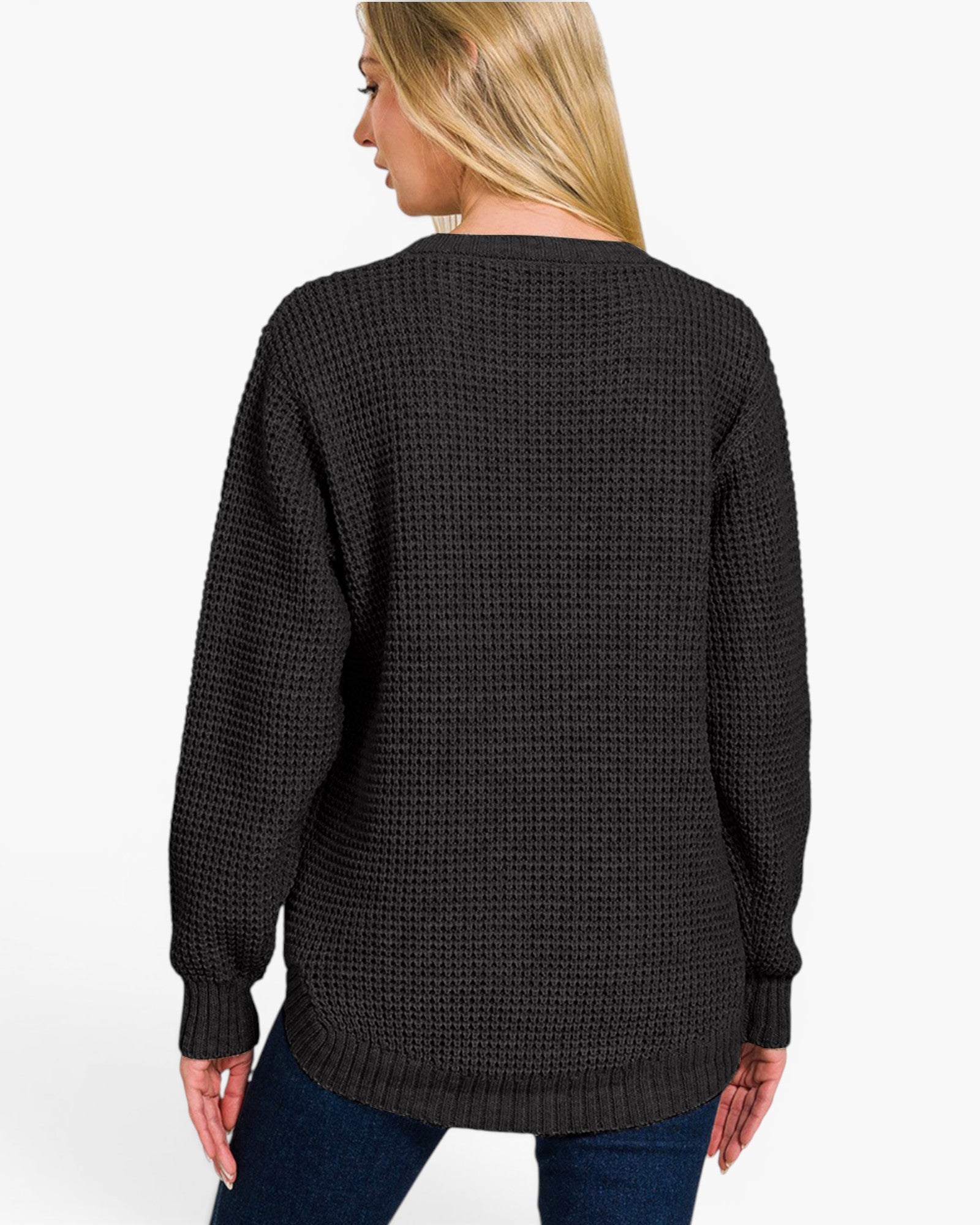 A woman shown from the back wearing a black waffle-knit sweater and blue jeans against a plain white studio background.