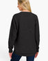 A woman shown from the back wearing a black waffle-knit sweater and blue jeans against a plain white studio background.