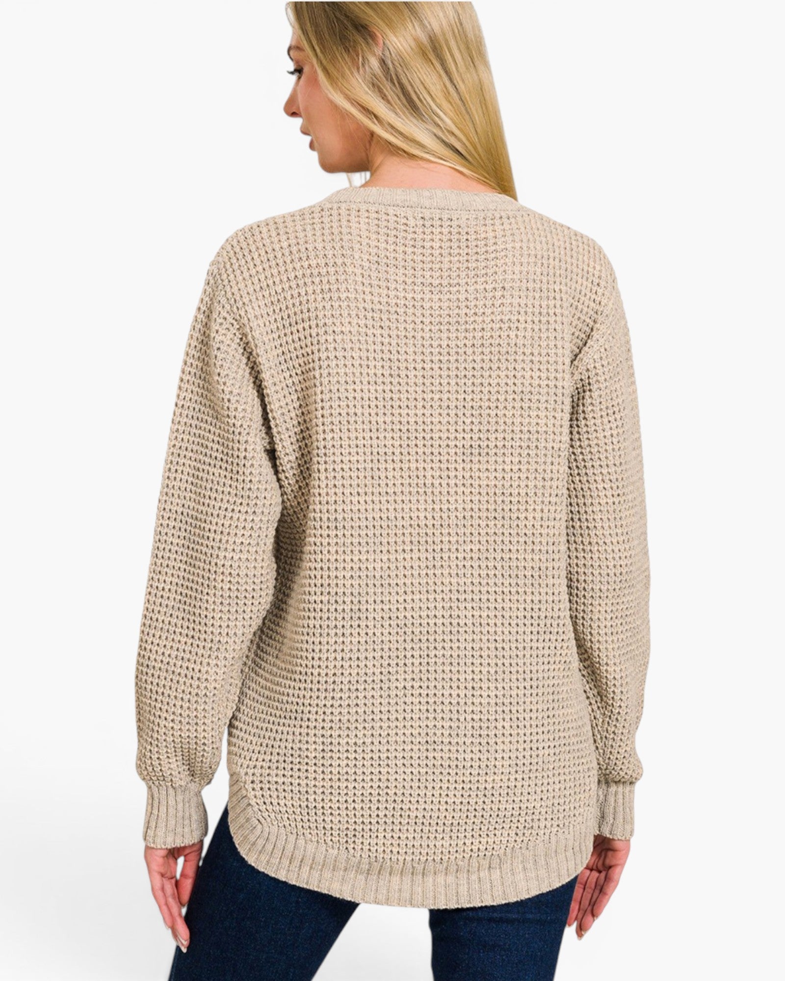 A woman shown from the back wearing a beige waffle-knit sweater and dark blue jeans against a plain white studio background.