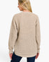 A woman shown from the back wearing a beige waffle-knit sweater and dark blue jeans against a plain white studio background.