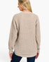 A woman shown from the back wearing a beige waffle-knit sweater and dark blue jeans against a plain white studio background.