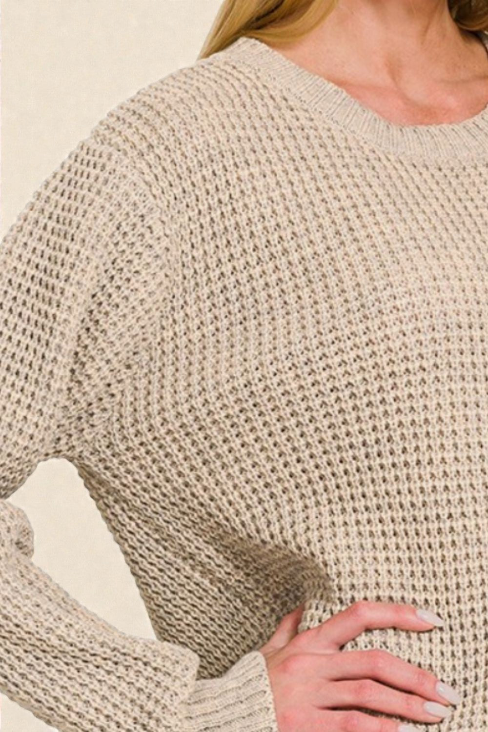 Close-up of a person wearing a beige knitted sweater on a light background