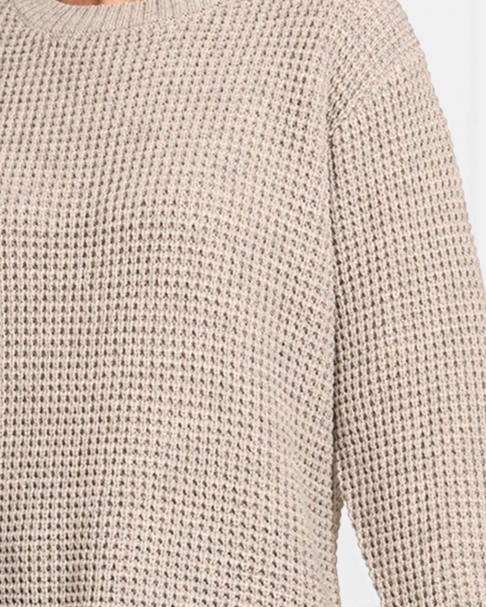 Close-up of a beige textured knit sweater with a ribbed crew neck and long sleeve, showing the detailed waffle-knit pattern.