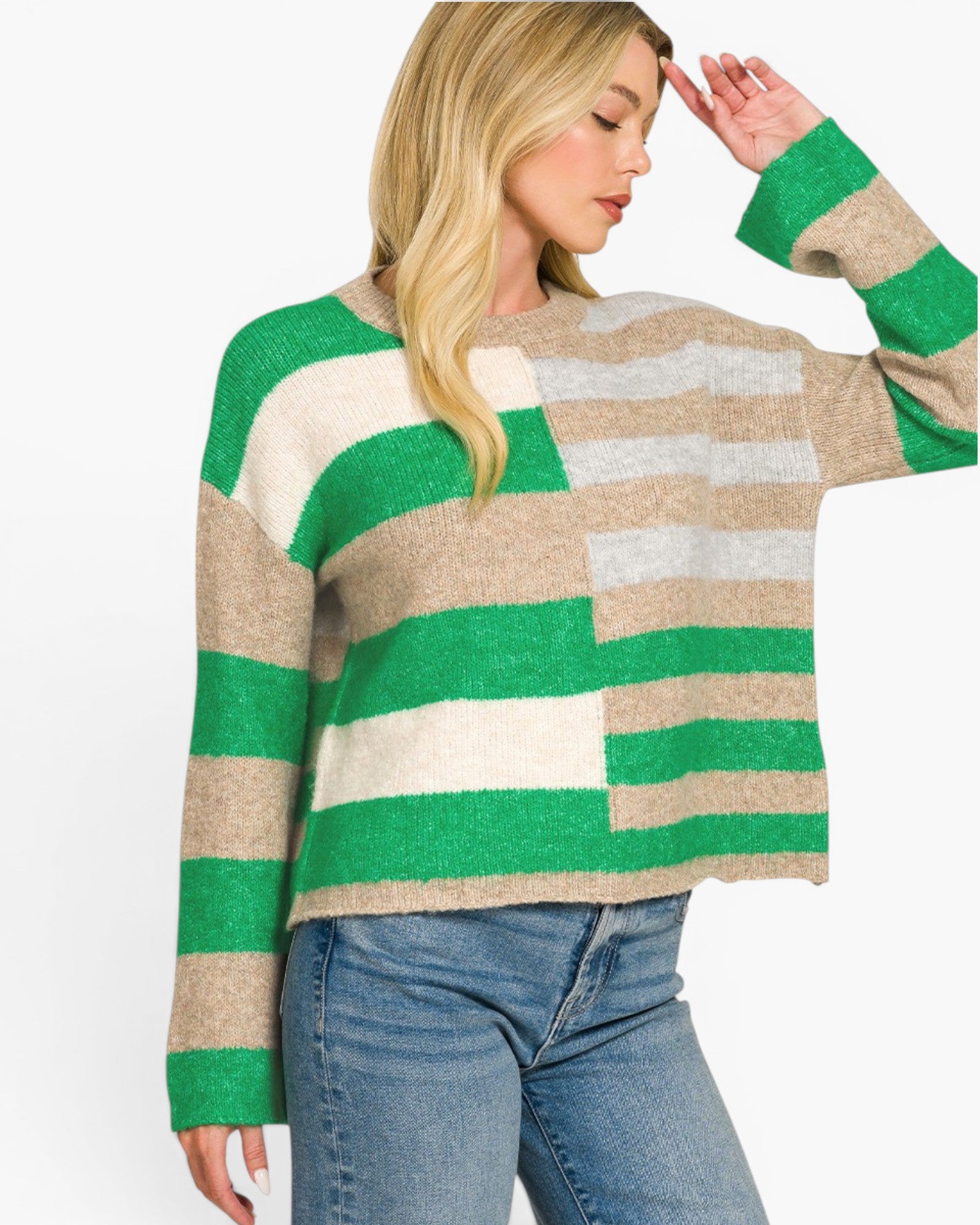A woman wearing a chunky knit sweater with horizontal stripes in green, beige, and light gray, paired with blue jeans, against a plain white background.