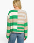 A woman viewed from the back wearing a knit sweater with wide horizontal stripes in green, beige, cream, and light gray, paired with blue jeans against a plain white background.