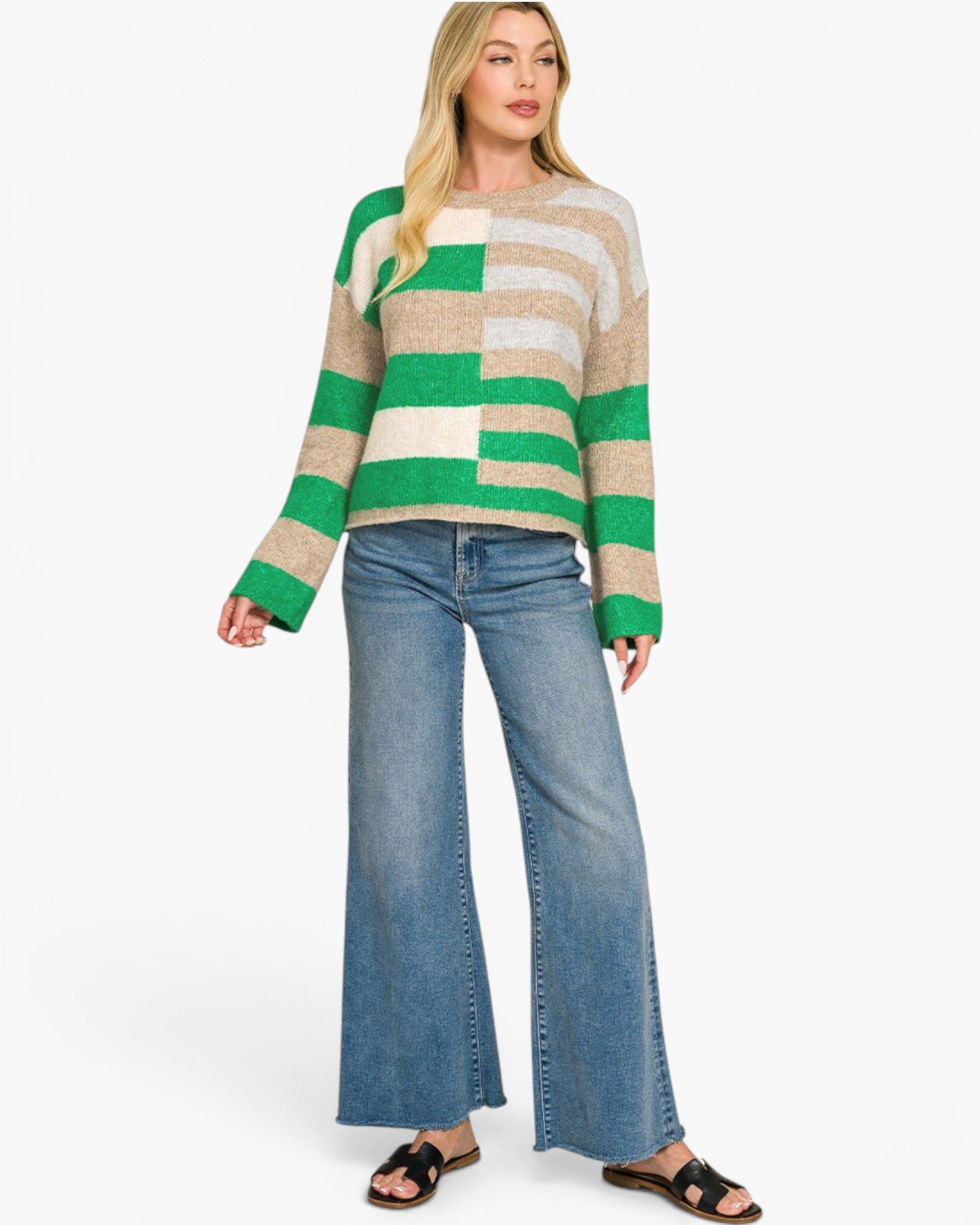 A woman modeling a green, beige, and white striped knit sweater paired with wide-leg blue jeans and black slide sandals, set against a plain white studio background.
