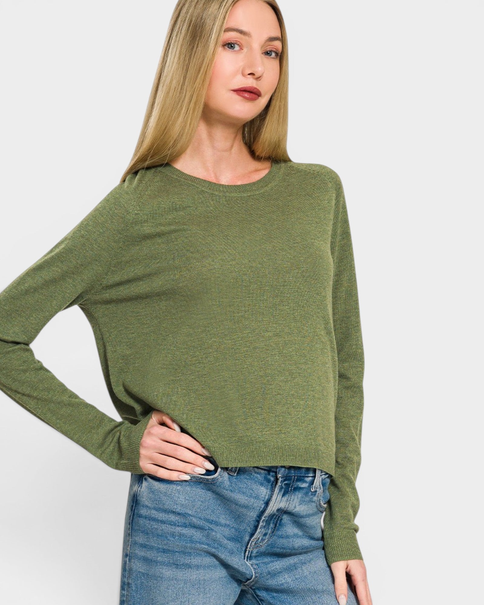 Woman wearing a green sweater and blue jeans on a white background