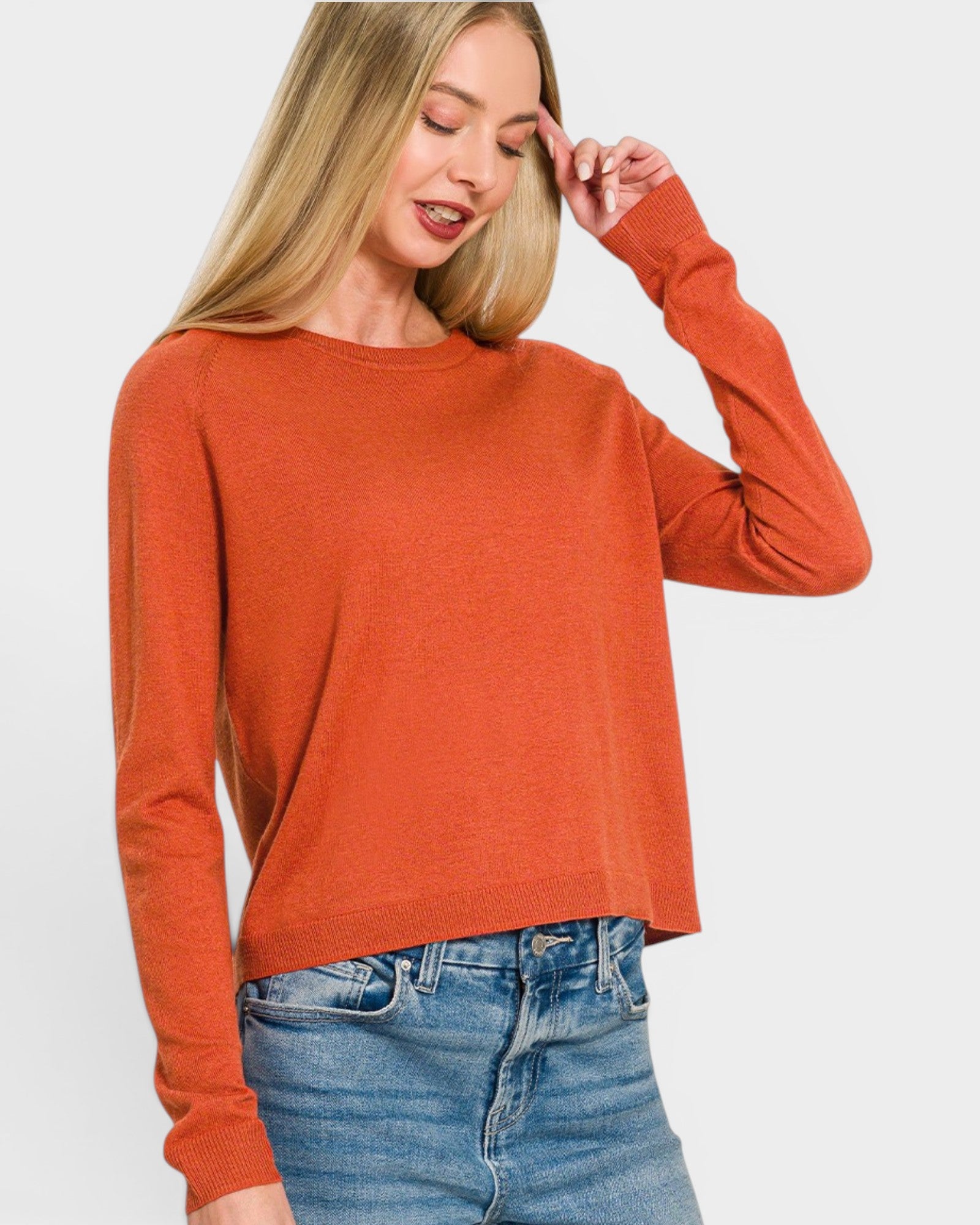Woman wearing an orange sweater and blue jeans on a white background