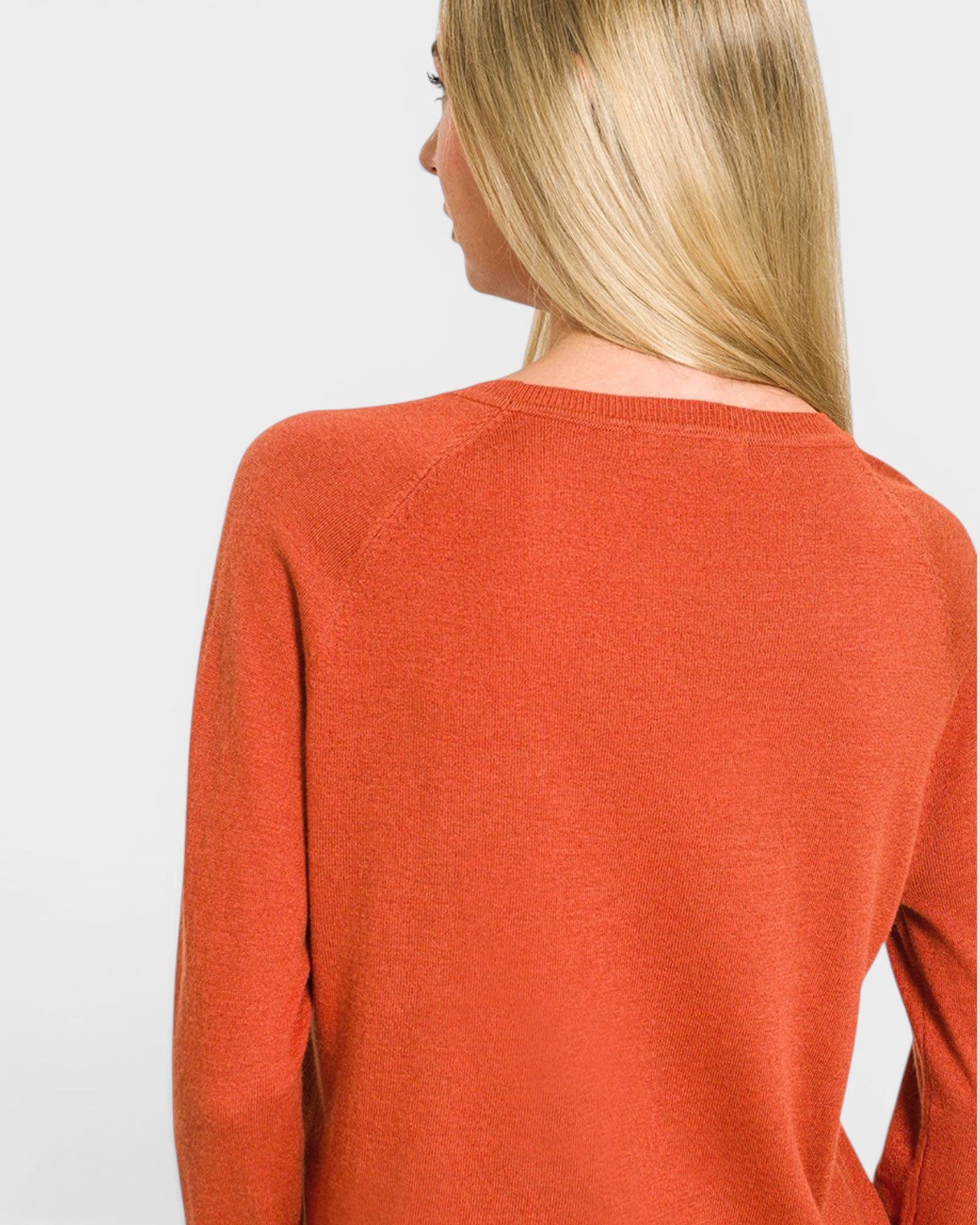 Person wearing a rust-colored sweater on a light gray background