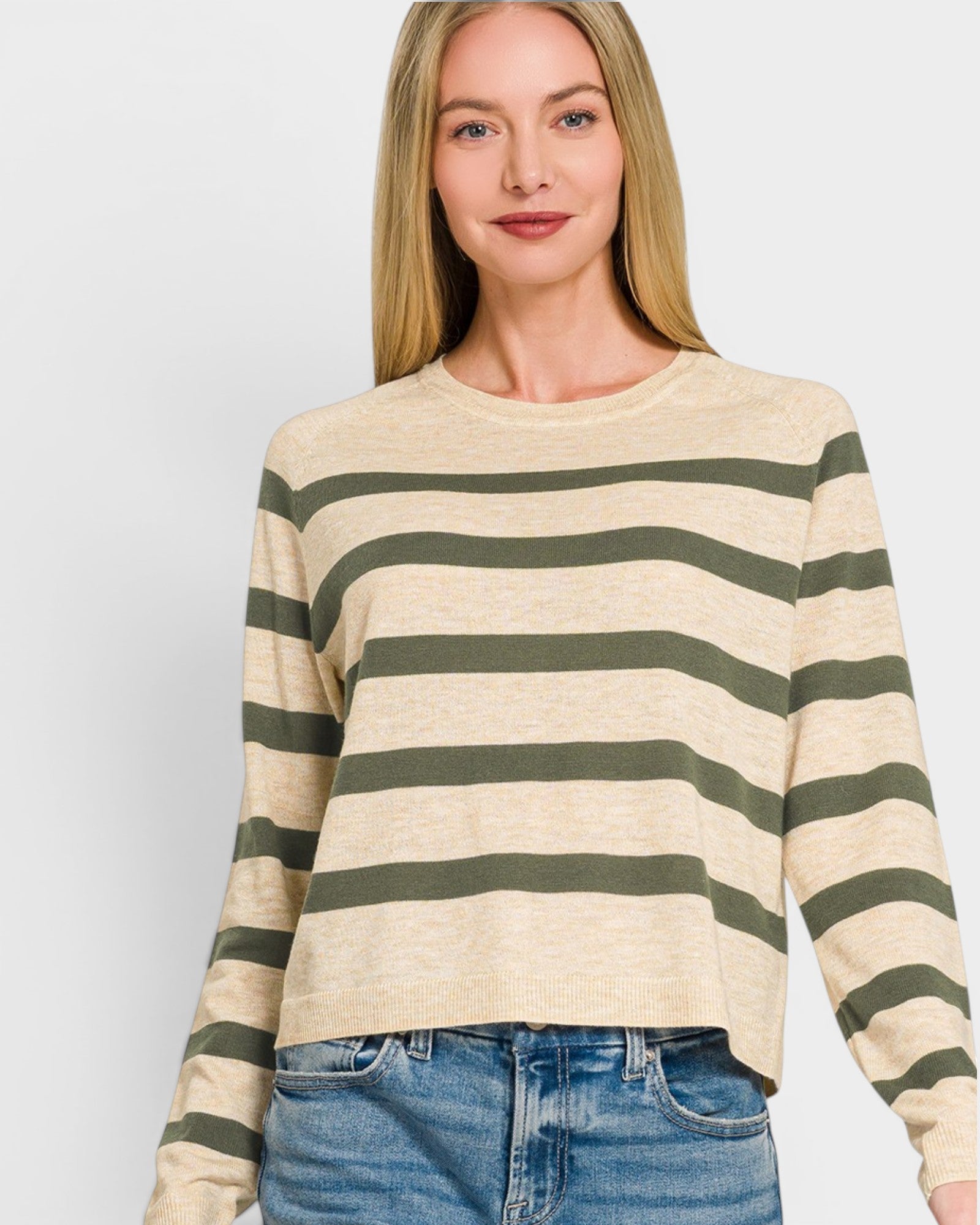 Woman wearing a beige and green striped sweater with blue jeans on a white background