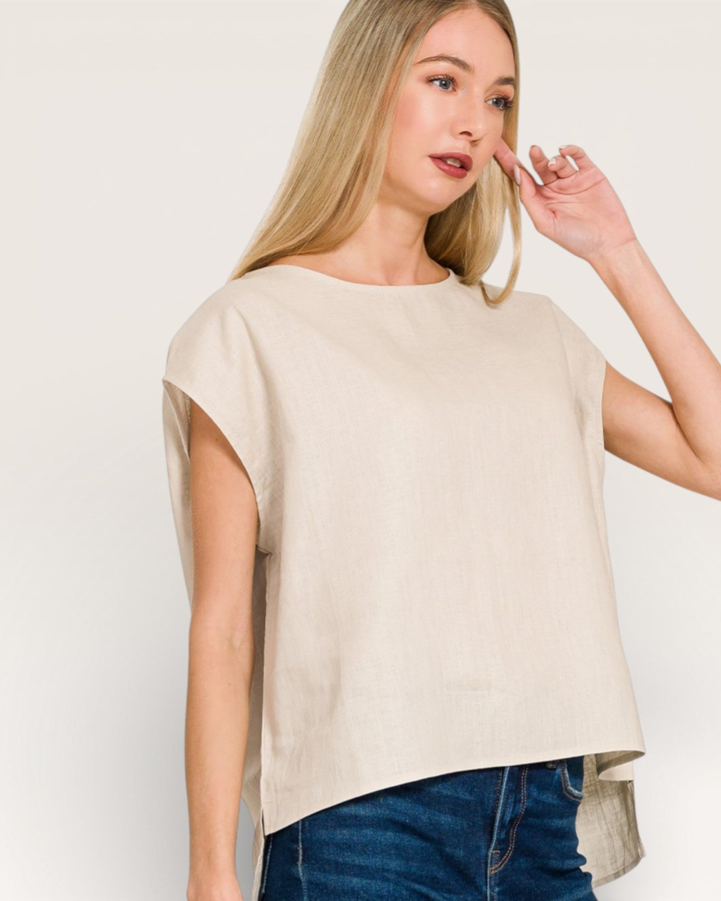 Woman wearing a beige top and blue jeans against a white background