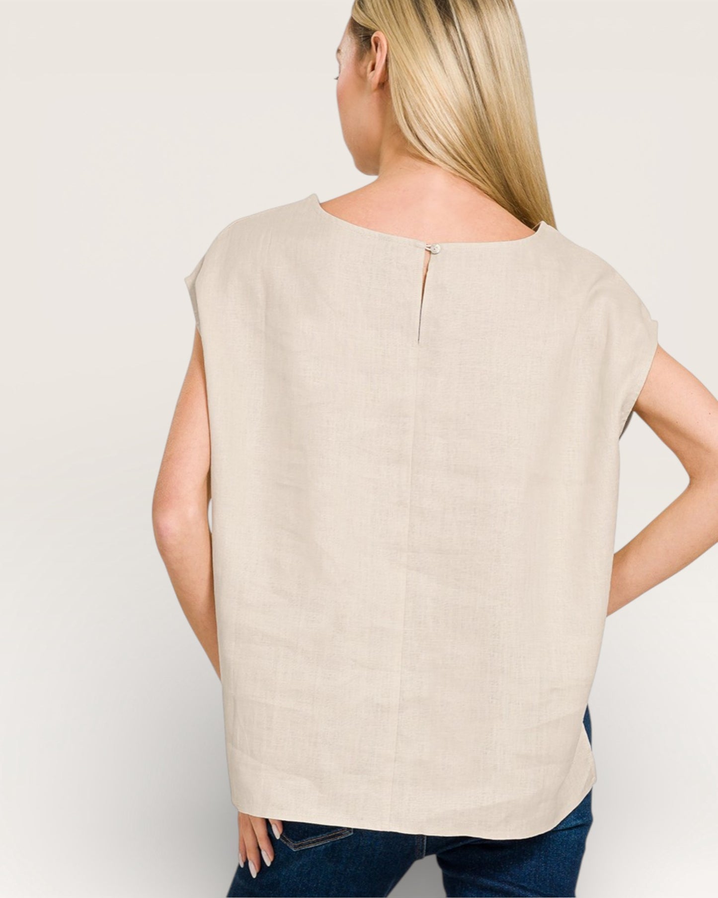 Woman wearing a beige sleeveless top against a plain background