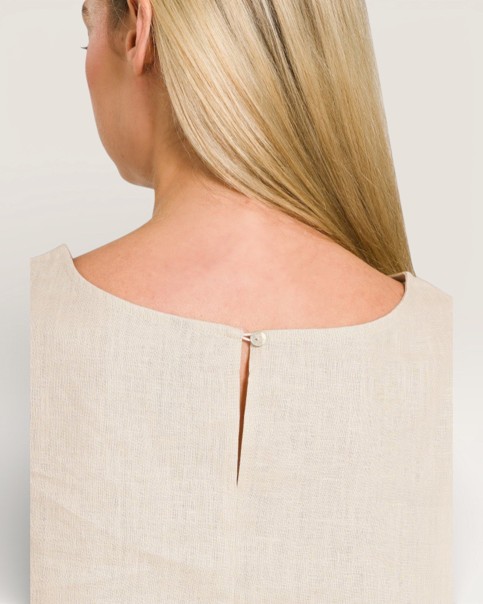 Close-up of a person wearing a beige top with a subtle cutout design on a plain background