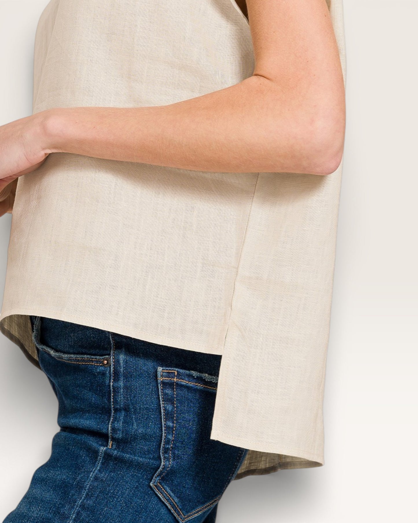 Person wearing a beige sleeveless top and blue jeans on a white background
