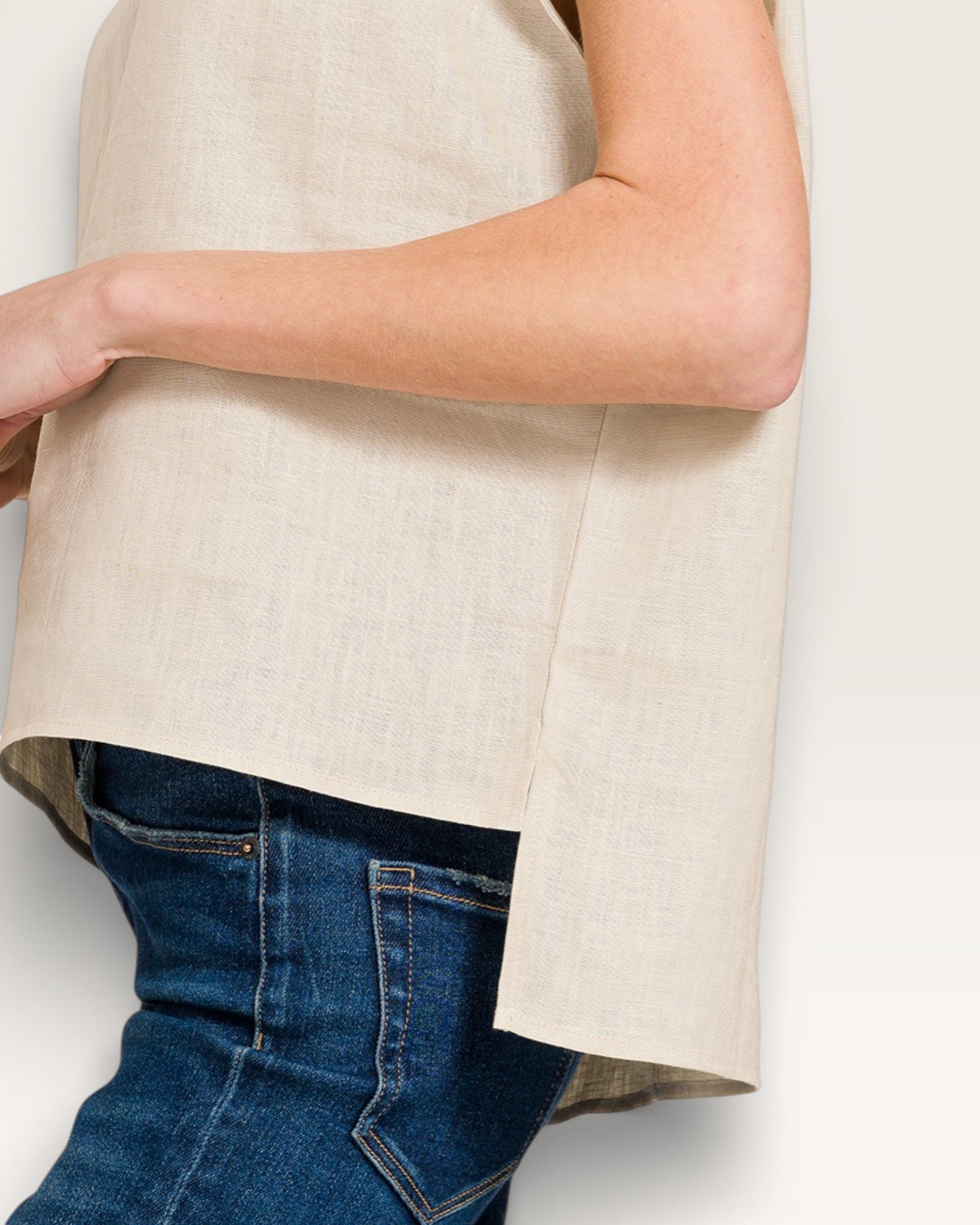 Person wearing a beige sleeveless top and blue jeans on a white background