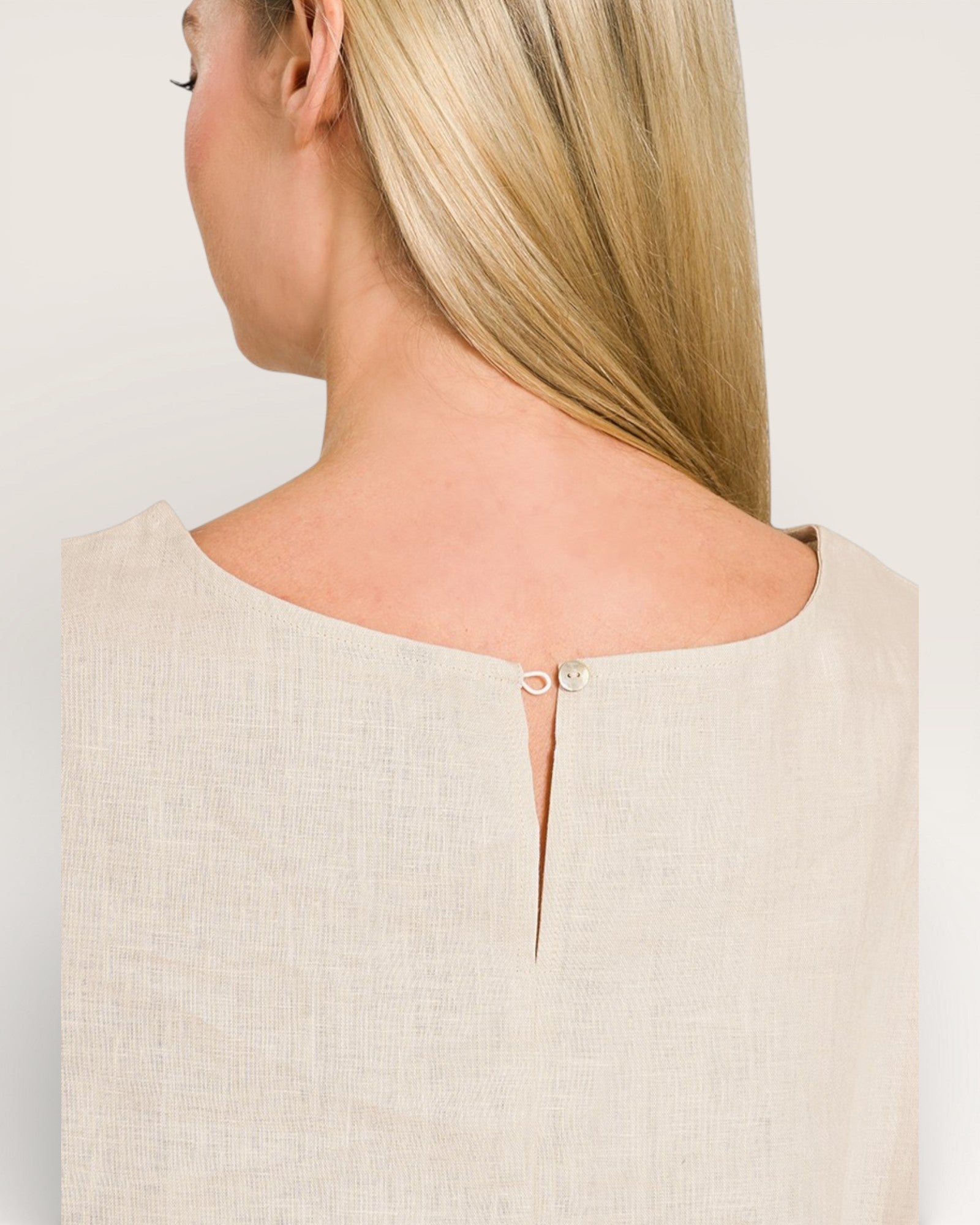 Woman wearing a beige sleeveless top with a subtle cutout design on a plain background