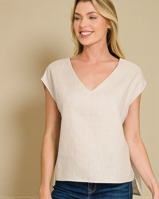 Woman wearing a beige cap sleeve top against a beige background