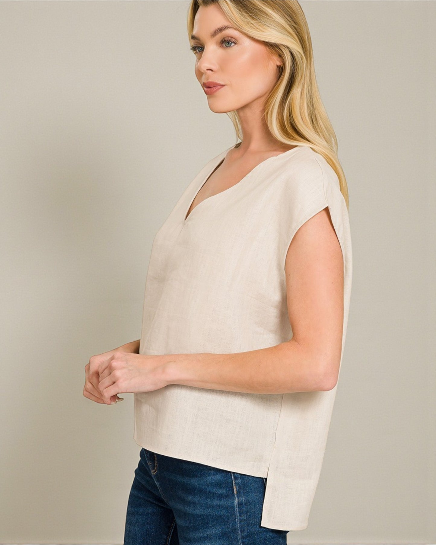 Woman wearing a beige sleeveless top and blue jeans against a plain background