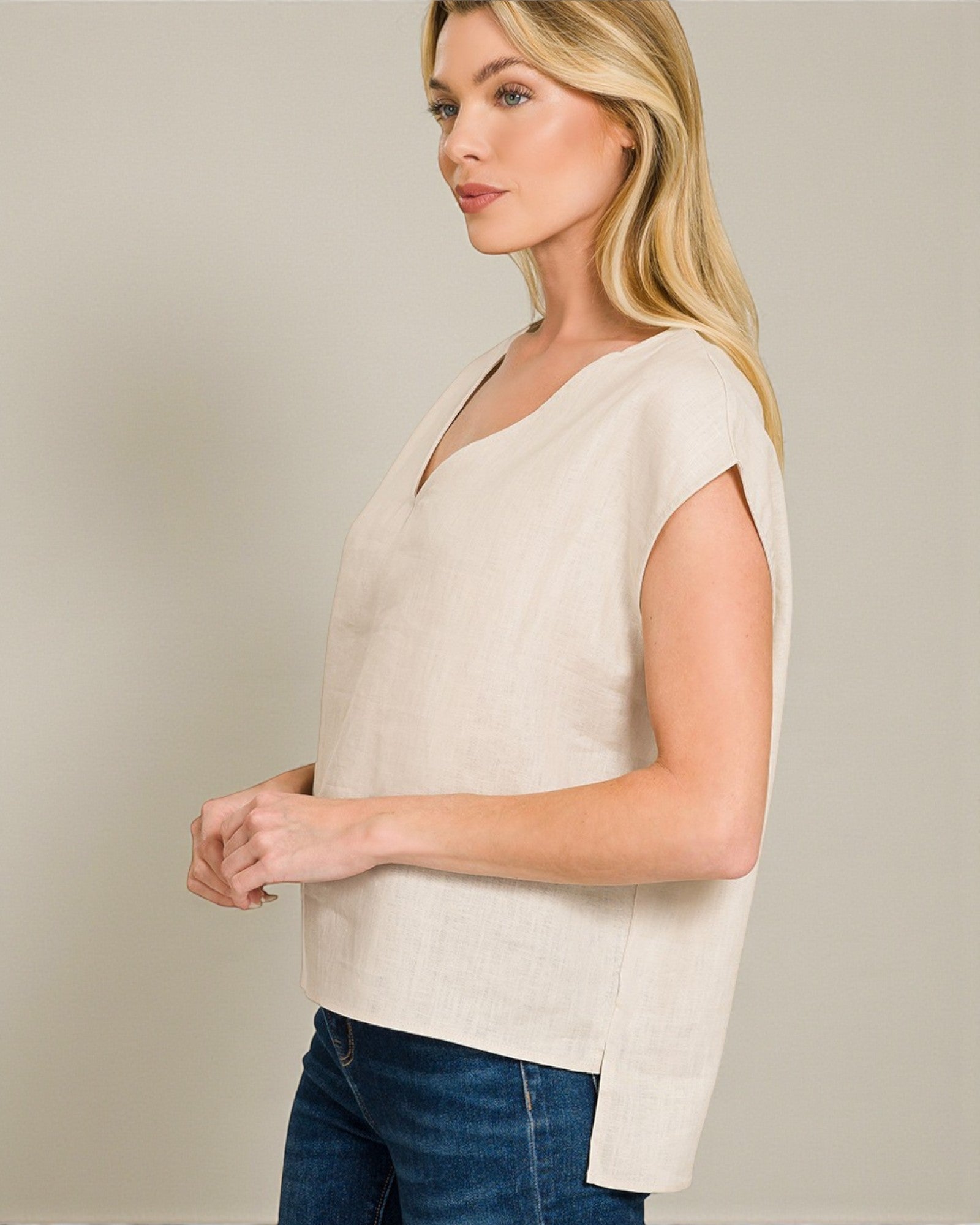 Woman wearing a beige sleeveless top and blue jeans against a plain background