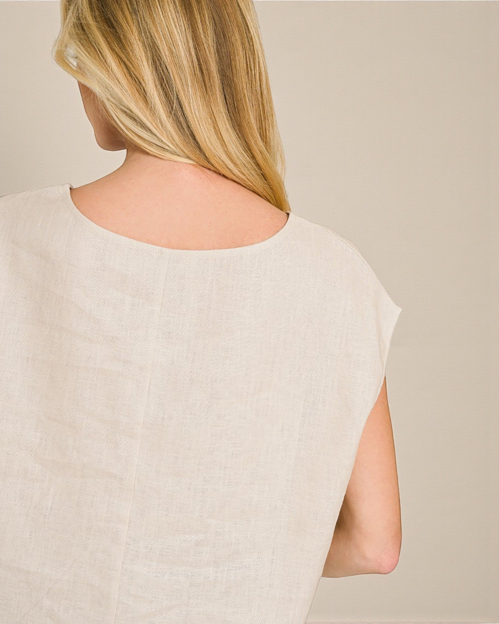 Person wearing a light beige sleeveless top against a neutral background