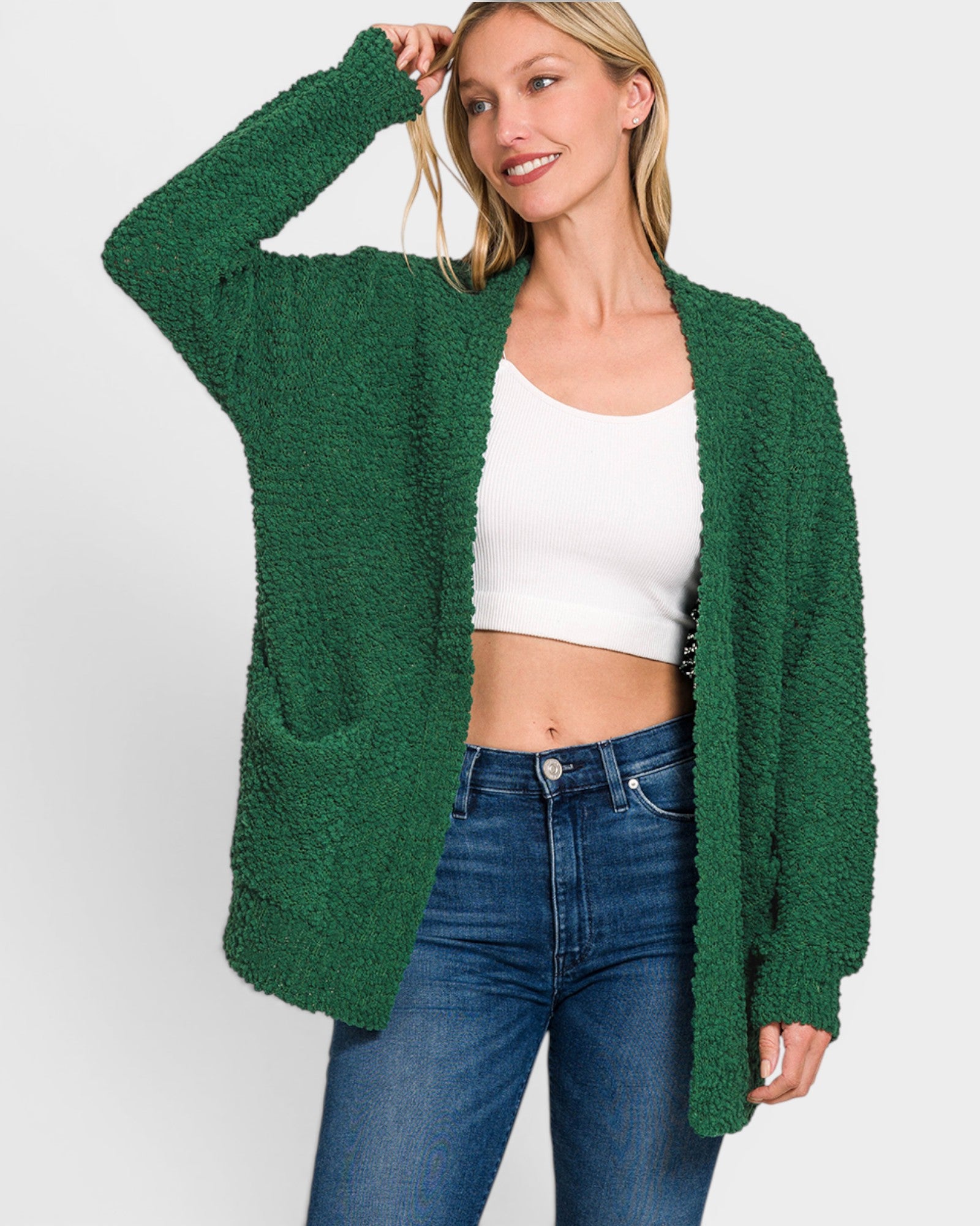 Woman wearing a green cardigan over a white top and blue jeans on a white background