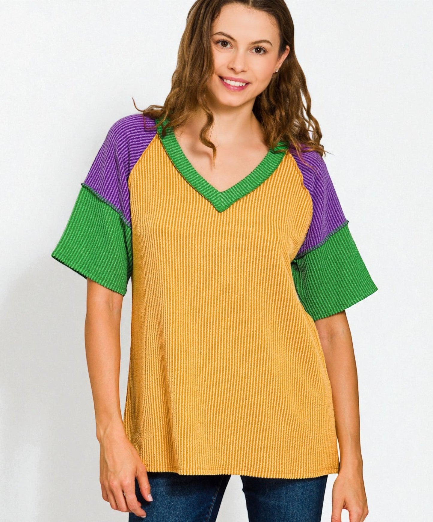 Woman wearing a mustard yellow sweater with green and purple sleeves on a white background