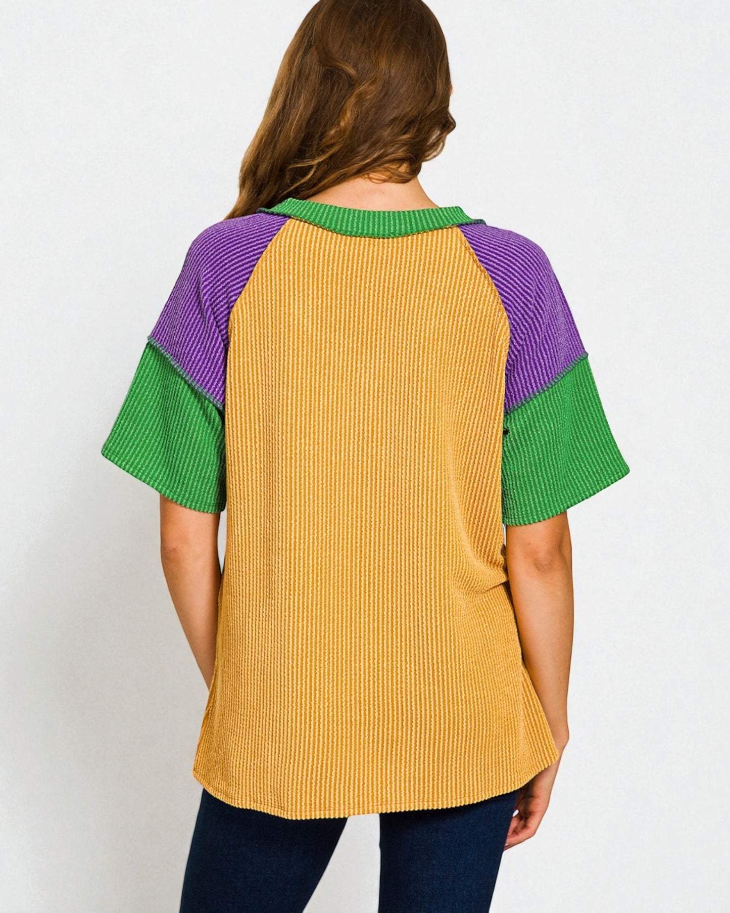 Woman wearing a mustard yellow ribbed top with green and purple sleeves on a white background