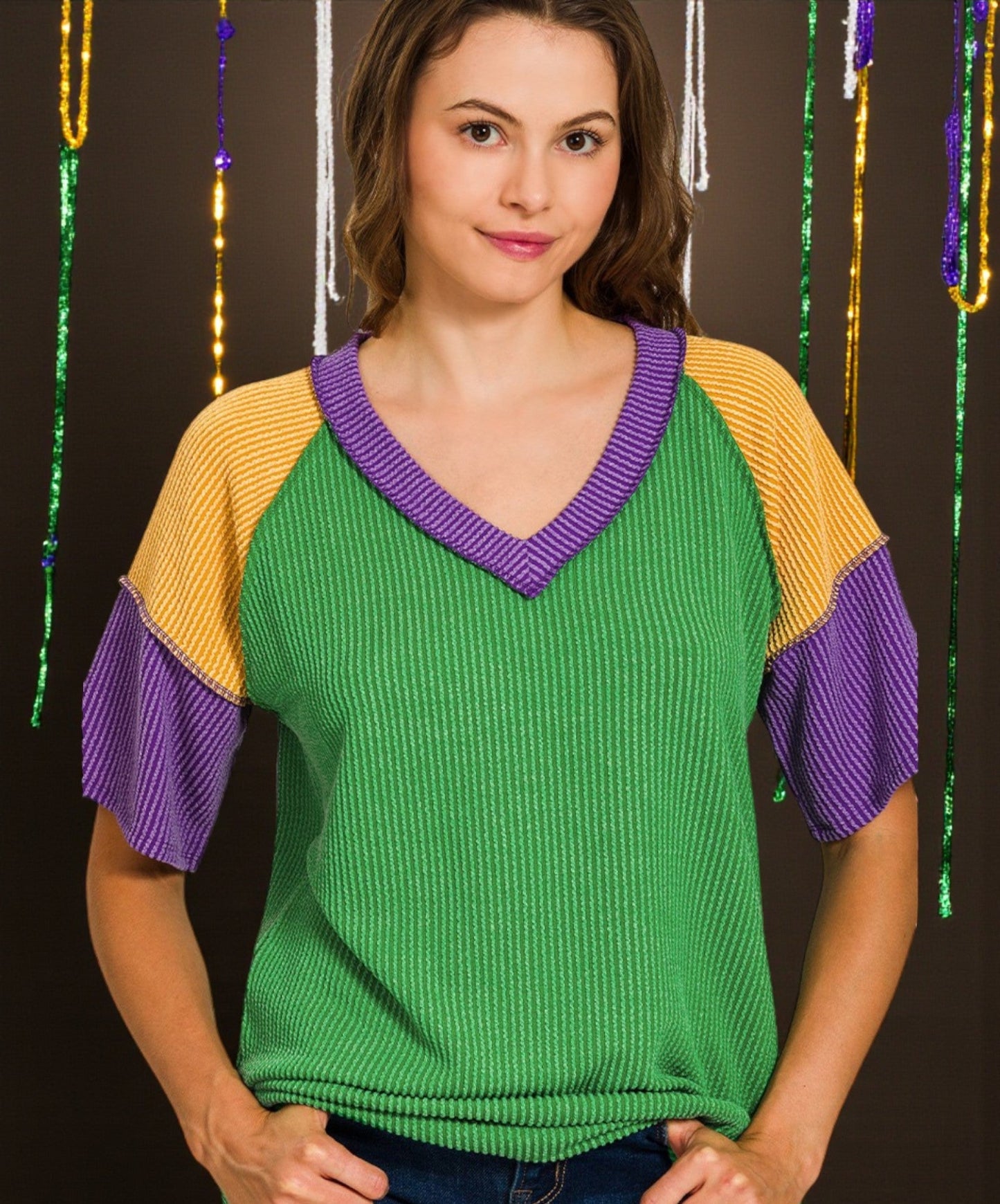 Woman wearing a green sweater with purple and yellow sleeves against a dark background