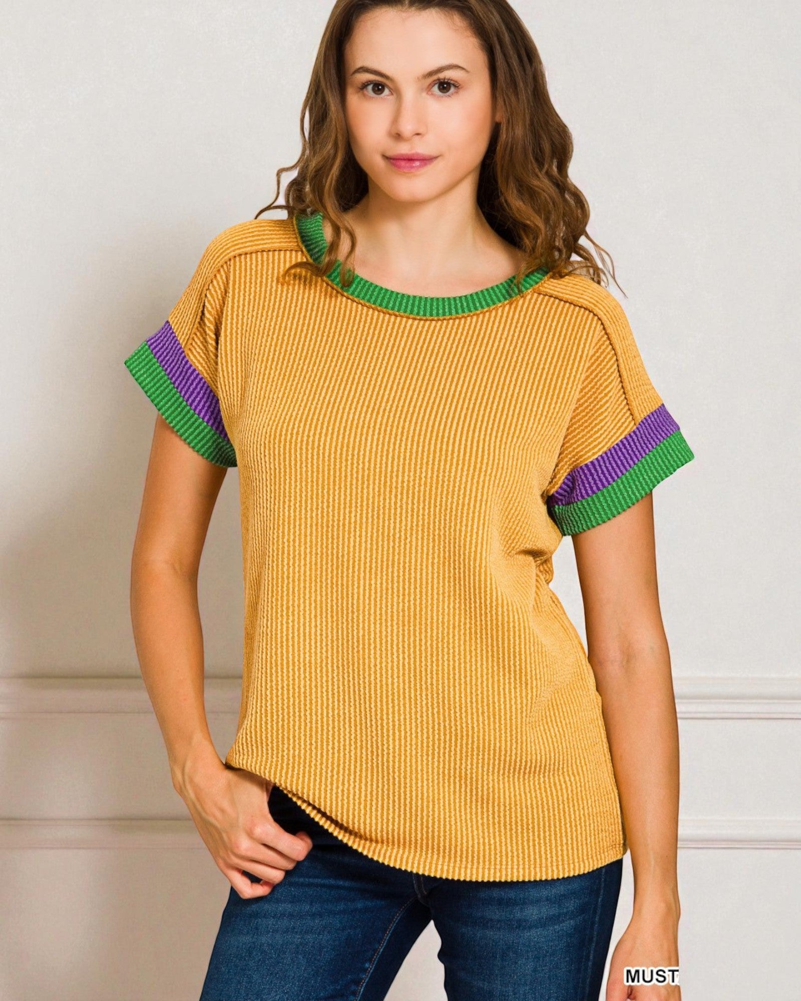 Woman wearing a mustard yellow top with green and purple sleeves against a neutral background