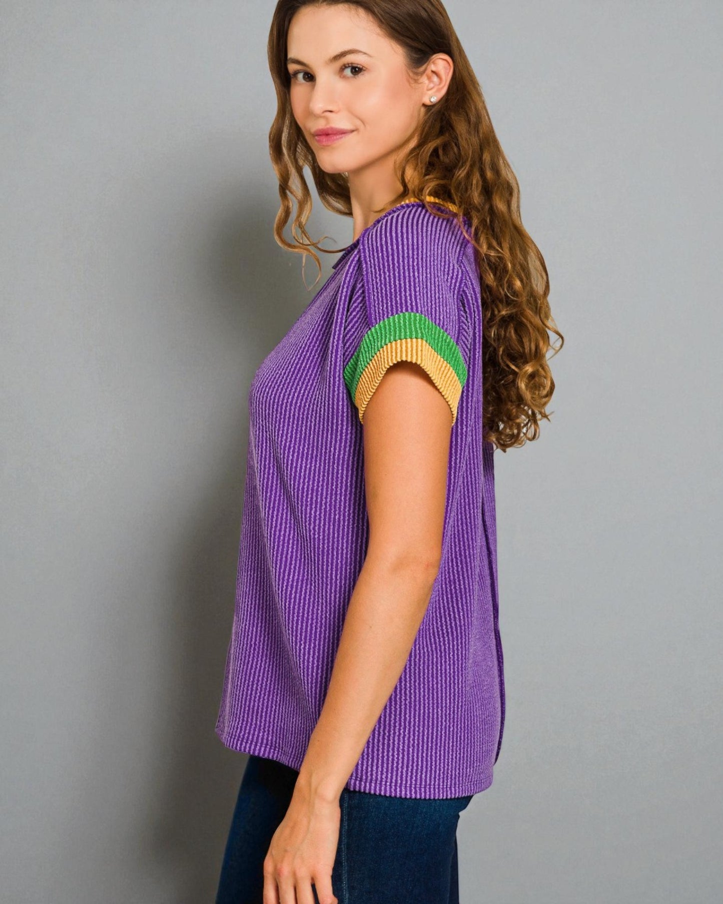 Woman wearing a purple ribbed sweater with green and yellow accents on a gray background