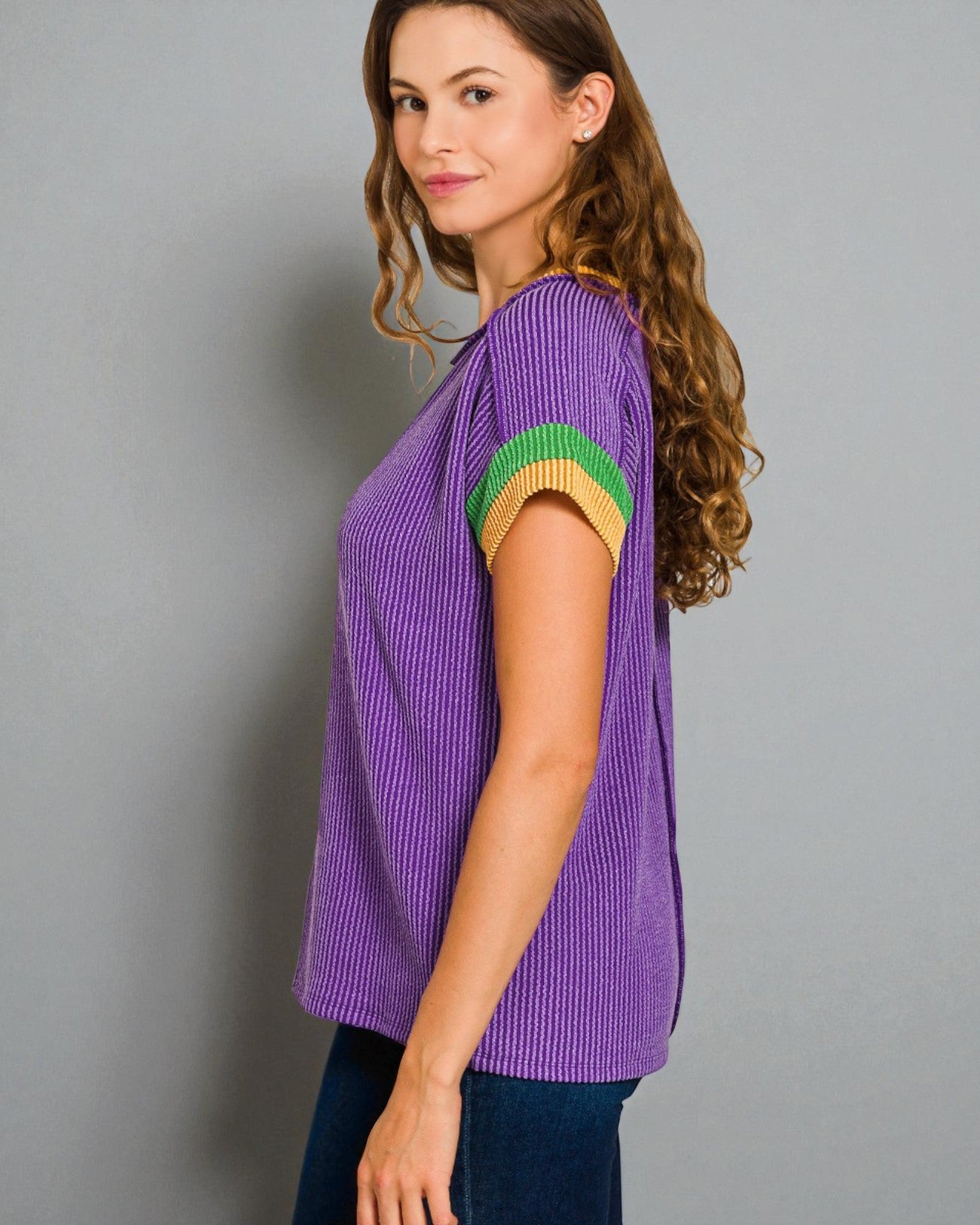 Woman wearing a purple ribbed sweater with green and yellow accents on a gray background