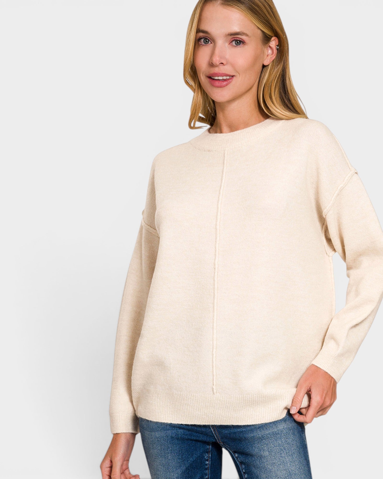Woman wearing a beige sweater and blue jeans on a light gray background