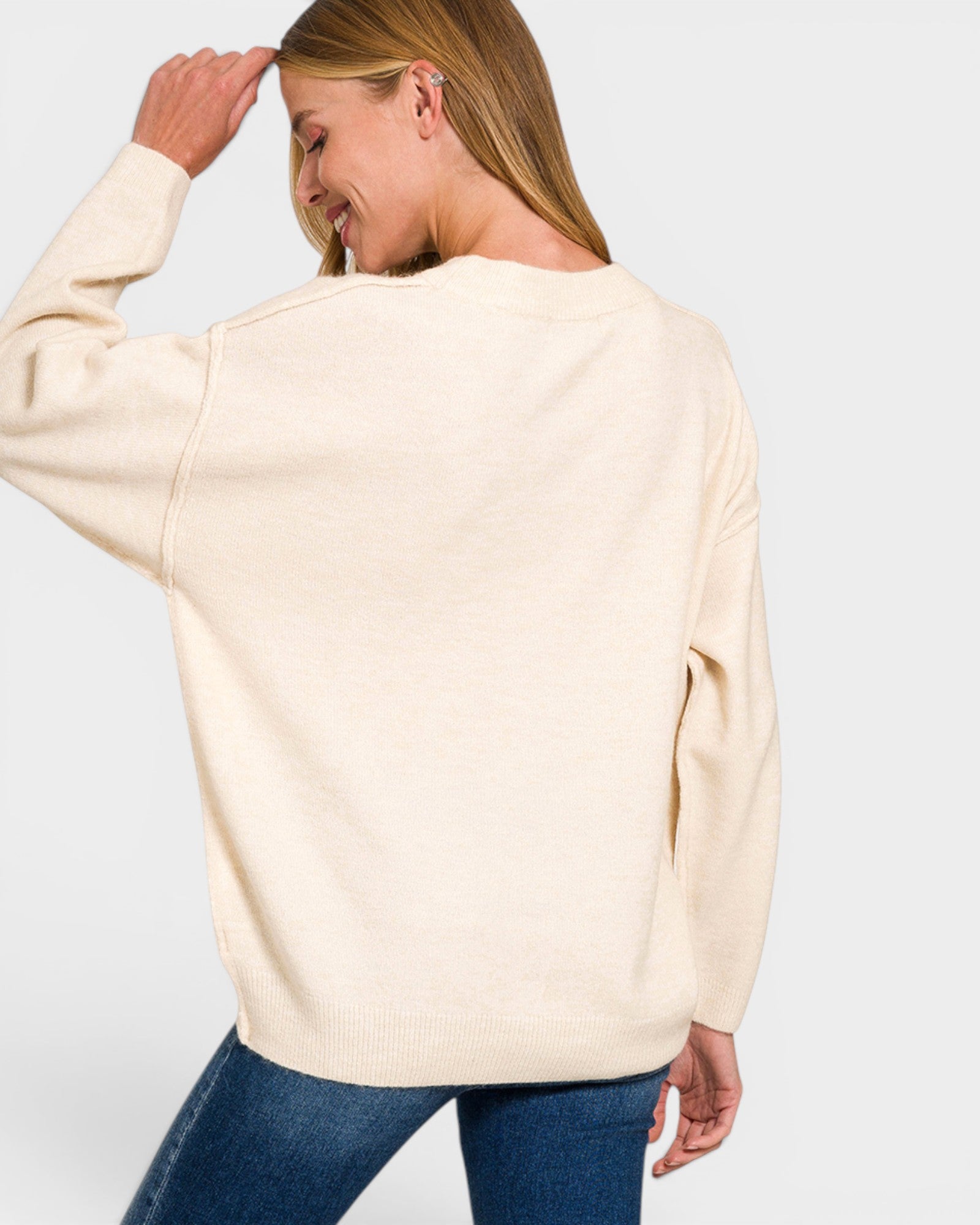 Woman wearing a beige sweater and blue jeans on a plain background