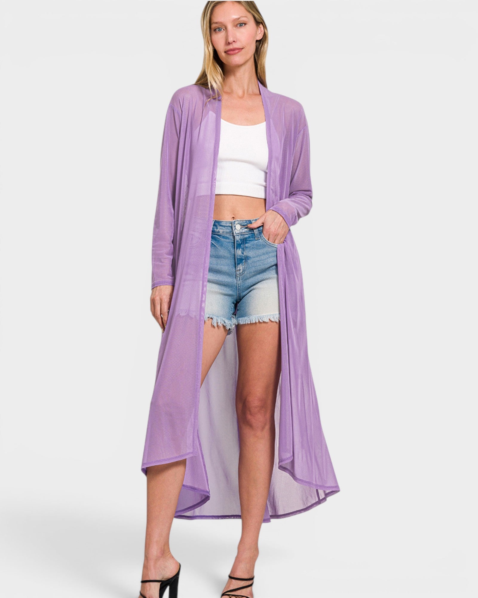 Woman wearing a long purple cardigan over a white top and denim shorts on a white background