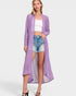 Woman wearing a long purple cardigan over a white top and denim shorts on a white background