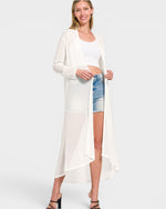 Woman wearing a long white cardigan over a white top and denim shorts on a white background