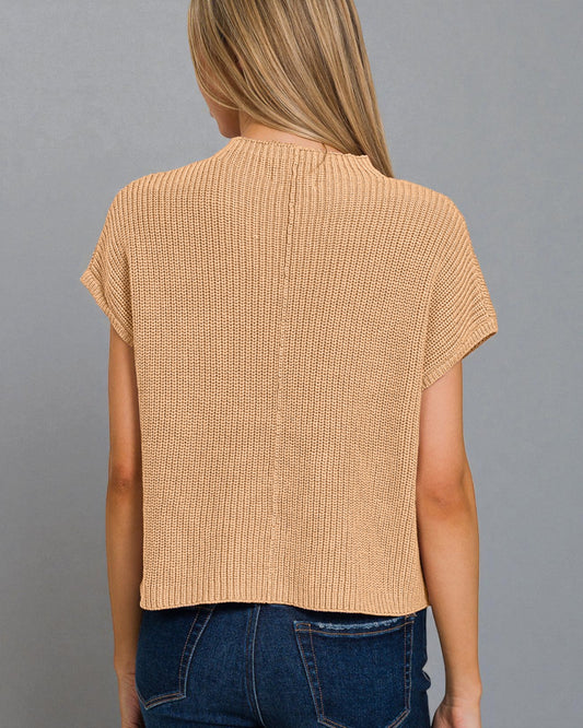 Woman wearing a beige knitted top and blue jeans on a gray background