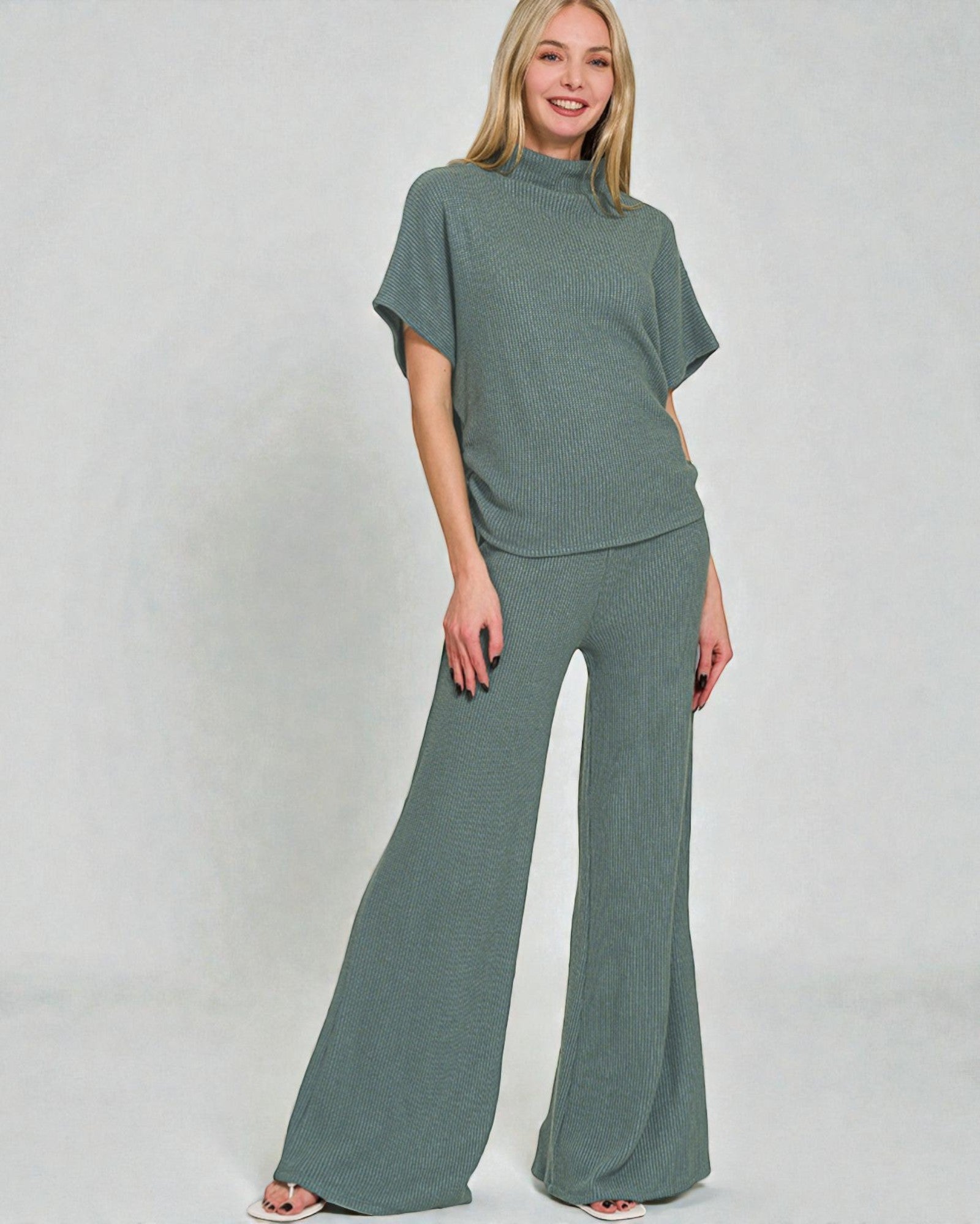 Woman wearing a green outfit with a top and wide-leg pants on a plain background