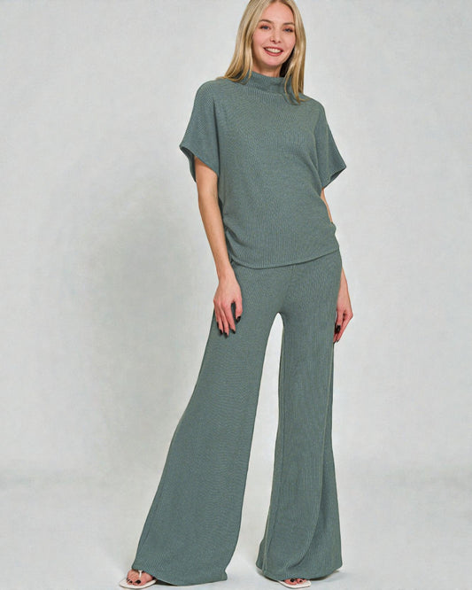 Woman wearing a green outfit with a top and wide-leg pants on a plain background